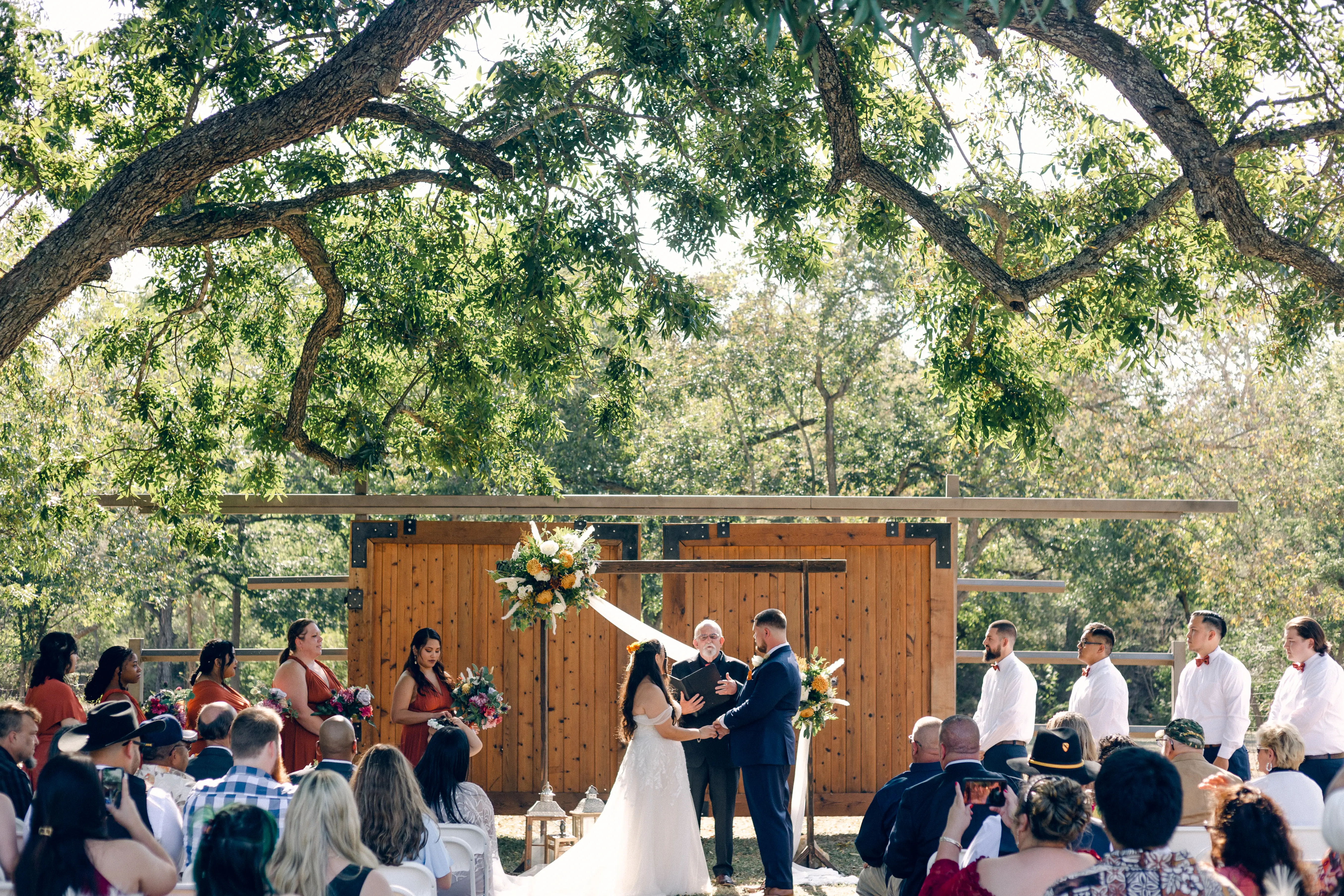 A bride and groom face each other while holding hands at the grand cedar doors under the pecan tree at hidden creek at stonehaus in belton