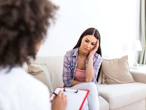 A woman appearing distressed sits on a couch while a therapist takes notes
