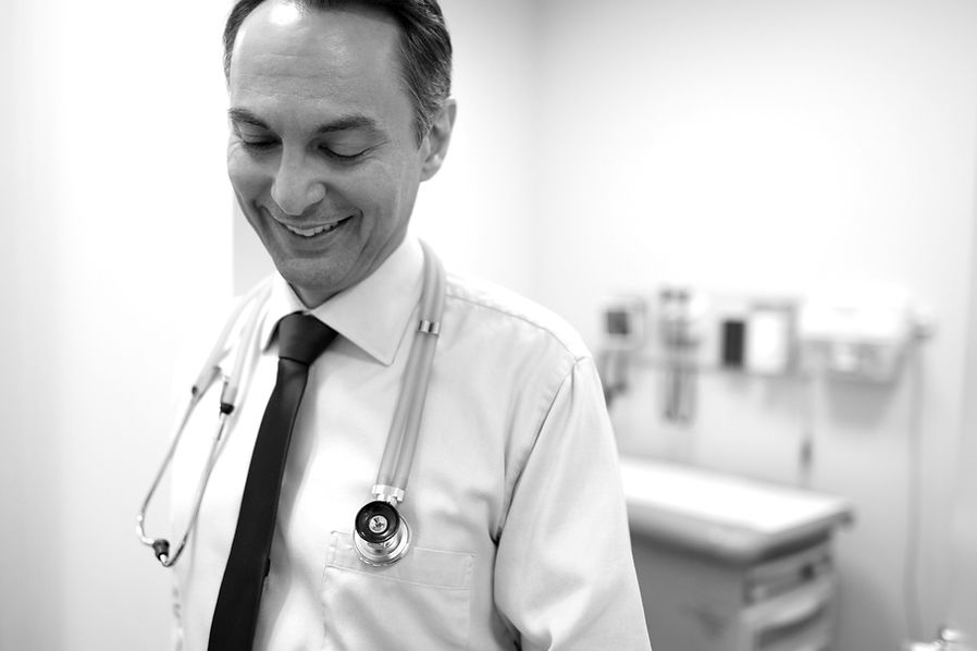 Doctor in white button down and dark tie with stethoscope hanging around his neck, he is smiling