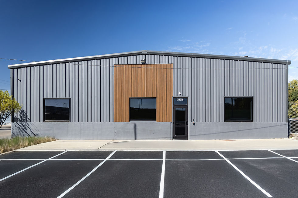 xterior of a renovated pre-engineered metal building with grey metal panel, a wood slat accent panel, black storefront windows and a painted concrete wainscot