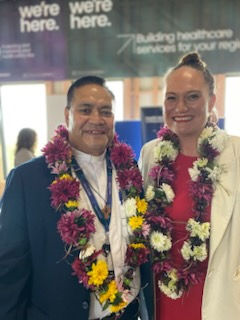 A man and a woman wearing formal attire and smiling with leis around their neck.