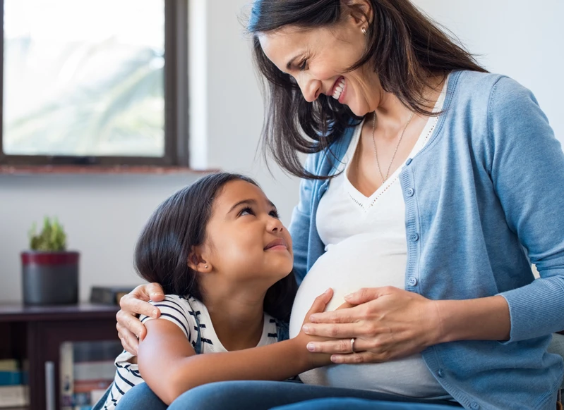 An expectant mom with her preschool child, embracing.