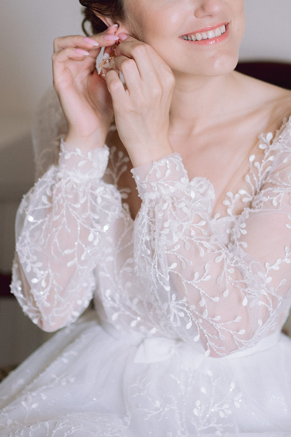 détail de la dentelle de la robe d'une mariée en train de mettre ses boucles d'oreille lors des préparatifs de son mariage
