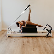 Pilates instructor is side lying on the long box with left leg looped up.