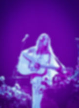 Singer-songwriter performing on stage with a guitar, microphone, and flowers; Playing in the Band.