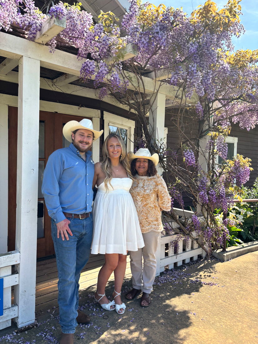 Saundra posing with a couple beneath a floral arch and chandelier, wine barrels lining the room behind them