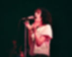 Patti Smith singing into microphone with her hands up on stage Playing in the Band