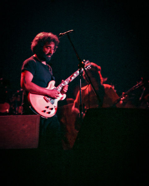 Jerry Garcia of Grateful Dead performing at Orpheum Theatre, San Francisco 1976, playing guitar on stage in front of microphone.