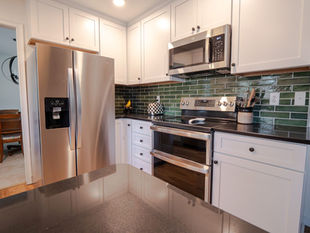 Bright modern kitchen with stainless steel fridge, stove, and microwave, white cabinets, green tile backsplash, and glossy black counter.
