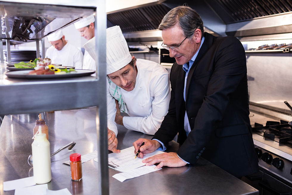 Male restaurant manager writing on clipboard while interacting to head chef in commercial