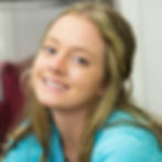 A portrait of a smiling woman with blue eyes and blonde hair, wearing a turquoise "Back to School" shirt, inside a room.