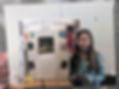 Girl in plaid shirt holds a school project board titled Christmas in Italy, with flags and photos, in a classroom setting.
