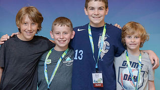 Four boys smiling with their arms around each other under a colorful balloon arch at an NSA event, standing in front of a banner that says 'If You Stutter, You Are Not Alone!