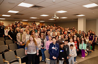Large group of National Stuttering Association (NSA) members and families posing together in a lecture hall.