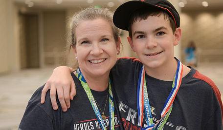 A smiling mom stands with her son, who is wearing medals and a lanyard, at an NSA event.