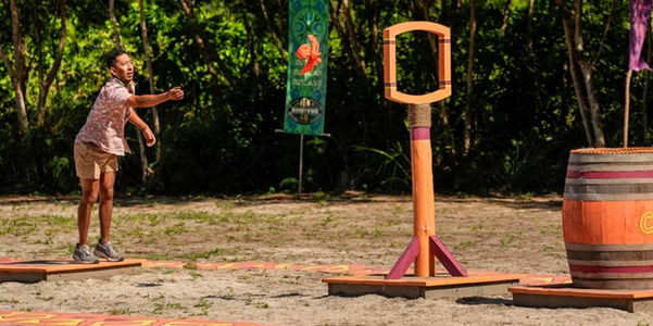 Mitch from the orange tribe throws a ring toward a wooden target in a precision-based challenge, with intense focus as part of the episode's competition segment.