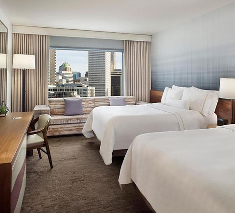 Modern hotel room with two queen beds and a city skyline view through the window.