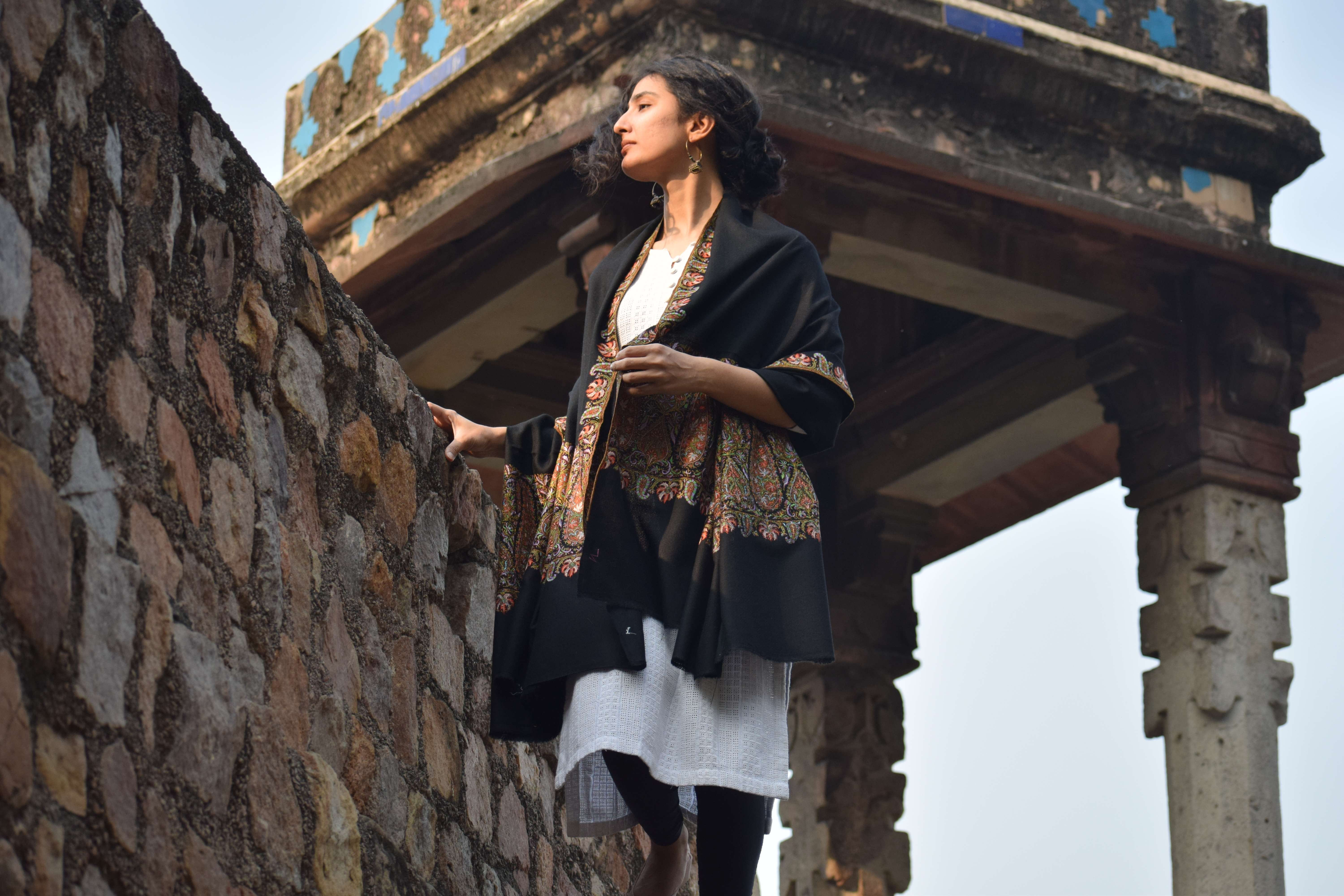 A woman in a black embroidered shawl at a stone pavilion in Kashmir