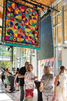 Visitors enjoying snacks and the company of their community under a rainbow tapestry.