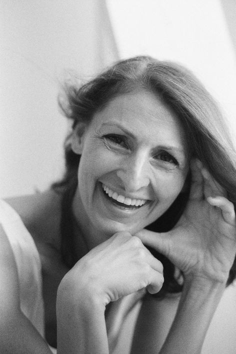 beautiful woman in her 40 smiling and holding her face gentrly with both her hands. wind in ther hair. studio portrait shoot in Basel