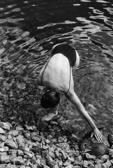 black and white photograph of woman by a rocky lake side beach