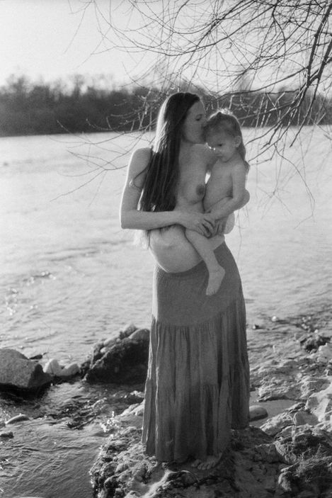 toddler in the arms of her pregnant mother by the river