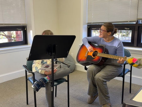 Photo description: Anne Frances (MTI) playing a guitar while a client holds a visual aid.
