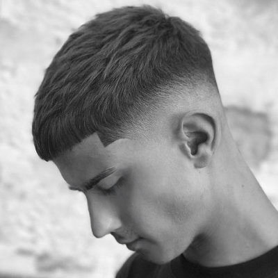 Side profile of a person with a neat short haircut, head tilted downward. The background is blurred, creating a calm, introspective mood.