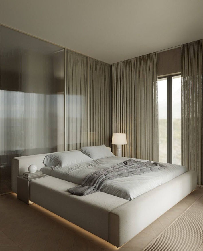 Minimalist bedroom with a low platform bed, soft neutral bedding, sheer curtains, and warm natural light.