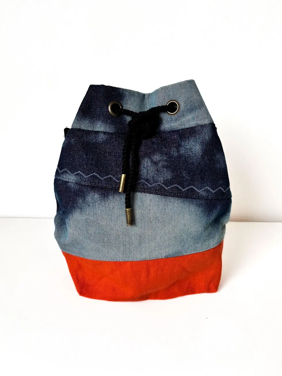Eine Bucket Bag aus gebatiktem Jeansstoff und einem Boden aus orangenem Canvas, steht vor einem weißen Hintergrund.