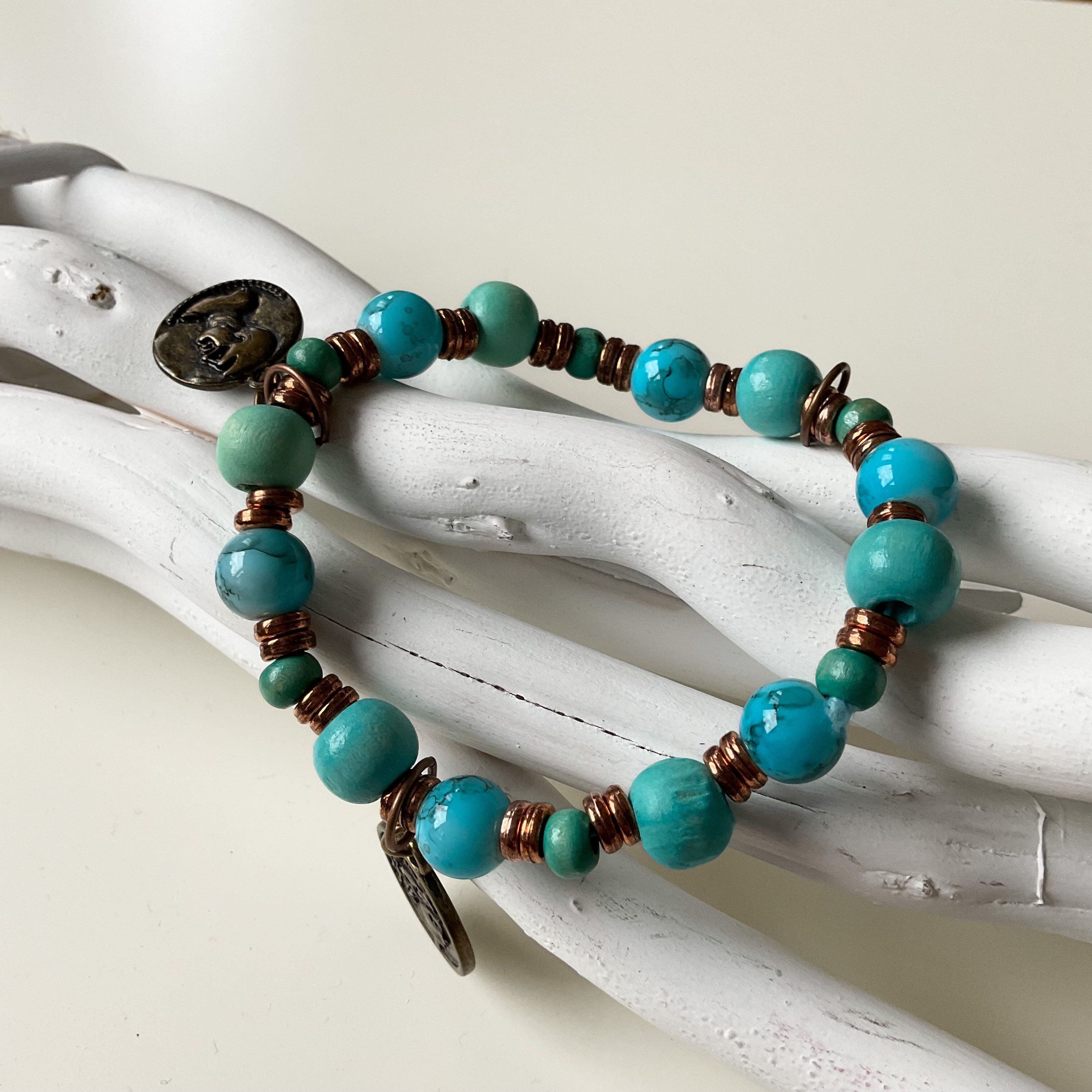 Auf dem Bild sieht man ein türkisfarbenes Perlenarmband, das dekorativ auf hellen, ineinander verschlungenen Holz- oder Treib