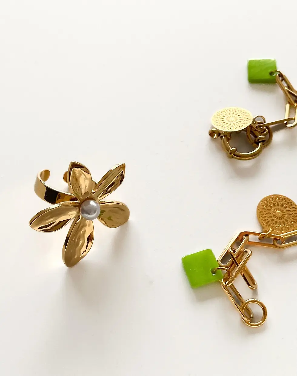 Miniaturbild: Vergoldetes Schmuckset mit einem Blumenring mit Perlenmitte und Kettenohrringen mit grünen quadratischen Akzenten und runden