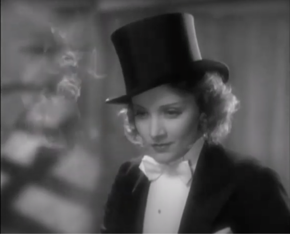 A person in a tuxedo and top hat looks down thoughtfully. Black and white setting with soft shadows in the background.