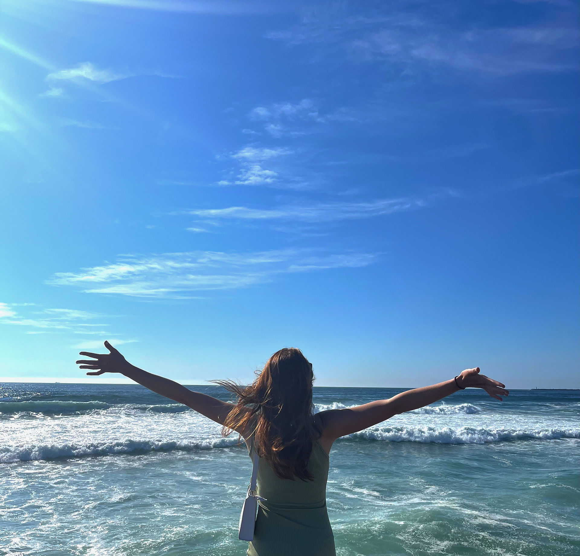 Back view of someone at Foz do Douro beach, arms raised, capturing the beauty of the vast Atlantic Ocean stretching into the horizon.