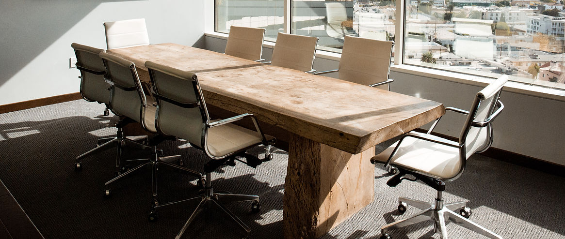 A long wooden conference table with six white office chairs in a bright room