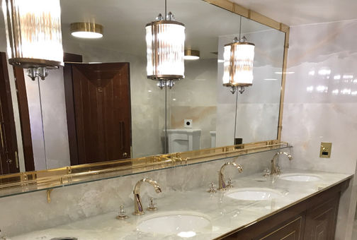 Luxurious bathroom with a large mirror, three sinks with gold faucets, and elegant pendant lights