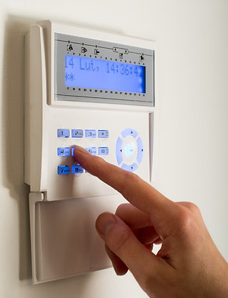 A person's hand presses buttons on a wall-mounted digital security keypad