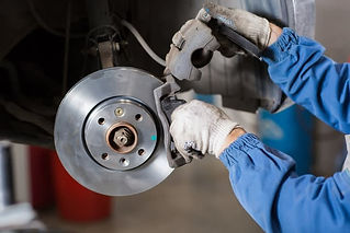 Mechanic in uniform inspecting car brake disc and caliper