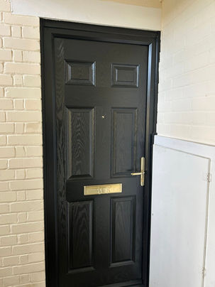 A black wooden door with a brass mail slot and handle, set in a cream brick wall