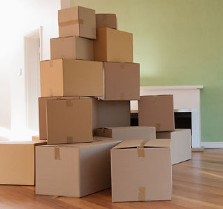 Stacked cardboard boxes fill a room with wooden floors