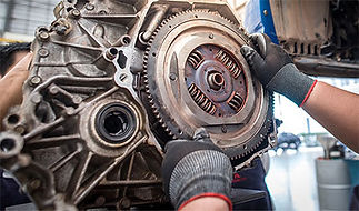 Mechanic wearing gloves works on a large metal engine, adjusting a round flywheel with visible gears and springs