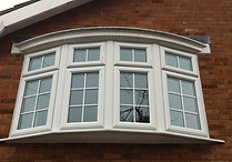 A white bay window with grid panes on a red brick house exterior