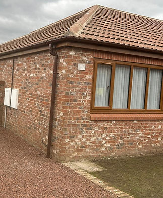 A single-story brick house with a sloped, red-tiled roof under a cloudy sky