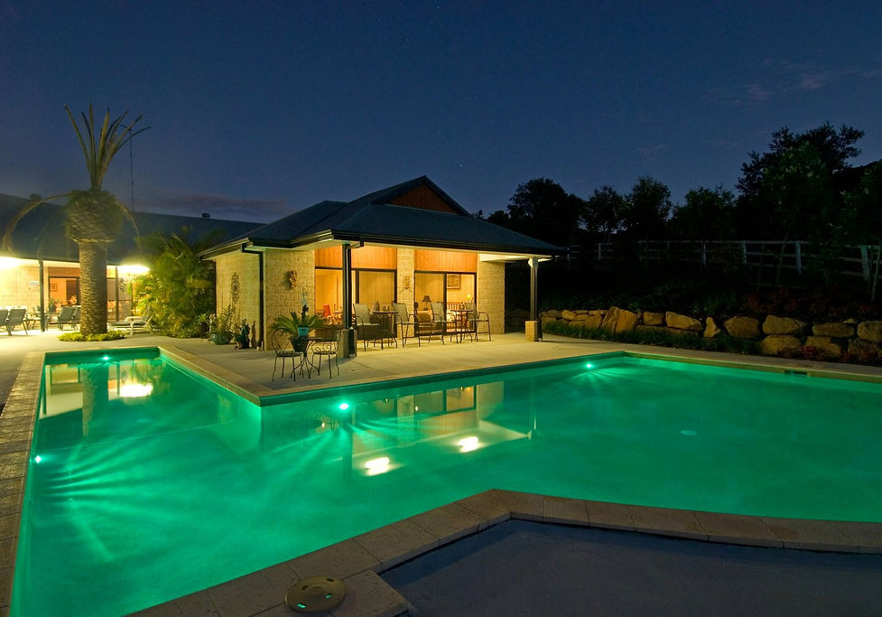 Night scene with glowing pool, illuminated house, and silhouetted trees