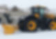 A yellow and black tractor plows snow in a residential area