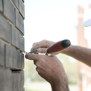 Person's hands using a chisel to repair brick wall mortar