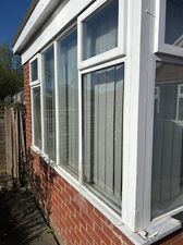 A Brick house exterior with large white-framed windows, showing wear.