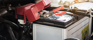 A car battery with a red jumper cable clamp attached to the terminal