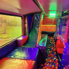 Interior of a colorful play area inside a vehicle, featuring padded seats, a slide, and a ball pit filled with red, blue, and orange balls