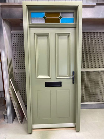 A sage green door stands upright, featuring a black handle and mail slot